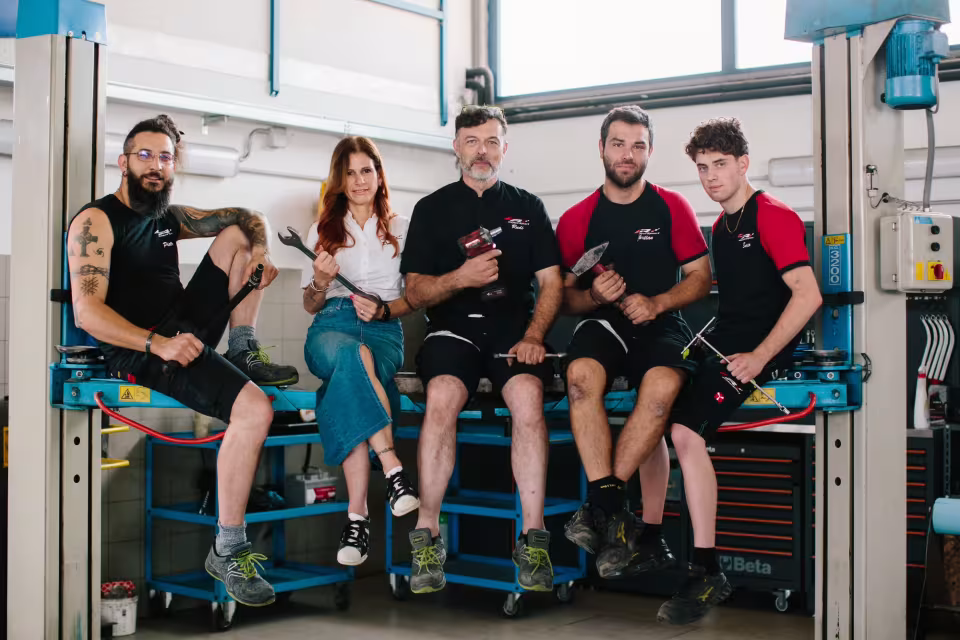 Il team dell'autofficina LR Motorsport nell'officina di Ponte nelle Alpi, seduto sul ponte sollevatore con gli attrezzi in mano